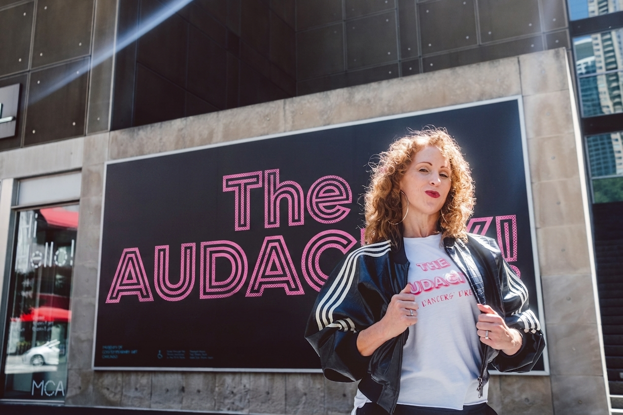 Mary Roberts in a leather jacket in front of The Audacity! mural